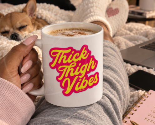 picture of a white coffee mug with the design thick thigh vibes resting on the crossed legs of the girl with a dog sleeping nearby