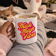 picture of a white coffee mug with the design thick thigh vibes resting on the crossed legs of the girl with a dog sleeping nearby